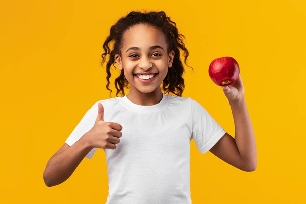 Πορτρέτο ενός χαρούμενου μαύρου κοριτσιού που κρατά κόκκινο μήλο - Φωτογραφία, εικόνα
