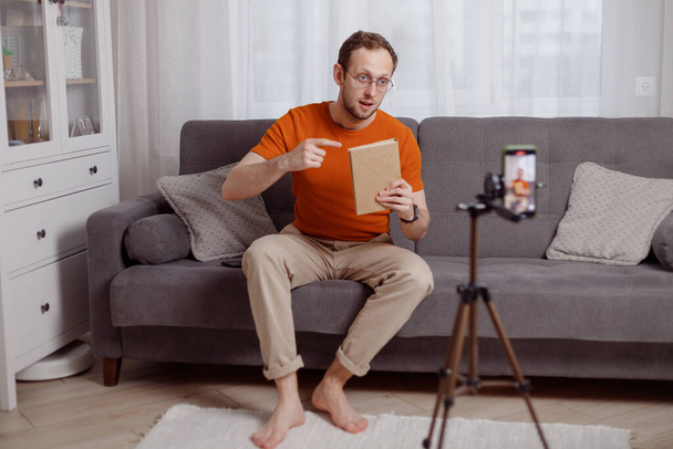 Schöner Mann Blogger zu Hause präsentiert Buch während Video-Stream. Social Media Marketing und Online-Verkauf - Foto, Bild