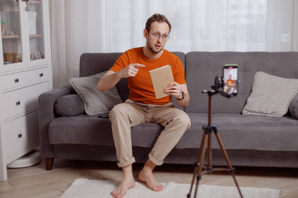 Όμορφος άνθρωπος blogger στο σπίτι παρουσιάζει το βιβλίο, ενώ ροή βίντεο. Μάρκετινγκ κοινωνικών μέσων και online πωλήσεις - Φωτογραφία, εικόνα