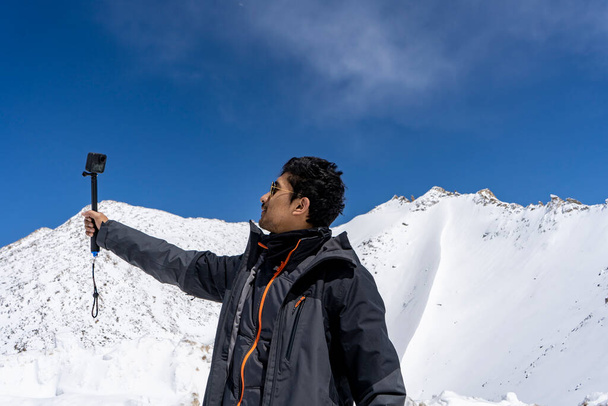 Młody i przystojny bloger męski podróży nagrywanie wideo do vlog z jego Go Pro kamery akcji, co vlog dla youtube w górach śniegu. - Zdjęcie, obraz