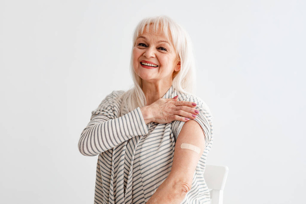 Glimlachende volwassen vrouw toont gevaccineerde arm na antivirale injectie - Foto, afbeelding