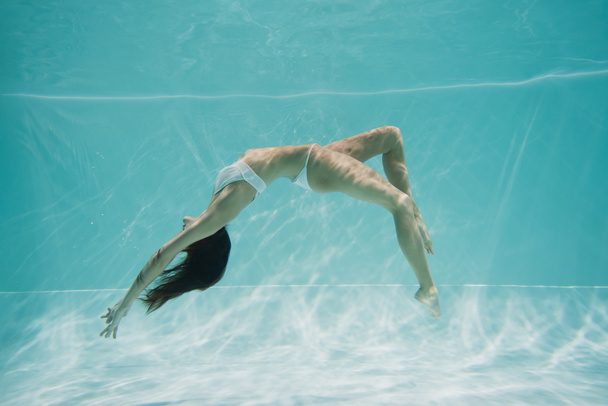 грациозная молодая женщина в белых купальниках плавает в бассейне  - Фото, изображение