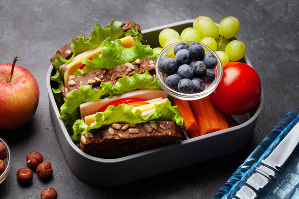 Healthy school lunch box with sandwich and fresh vegetables, water bottle, nuts and fruits - Photo, Image