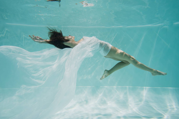 χαριτωμένη γυναίκα σε λευκό φόρεμα κολύμπι στην πισίνα  - Φωτογραφία, εικόνα