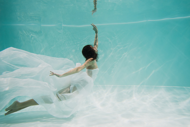 κομψή νεαρή γυναίκα με λευκό φόρεμα που κολυμπά στην πισίνα  - Φωτογραφία, εικόνα