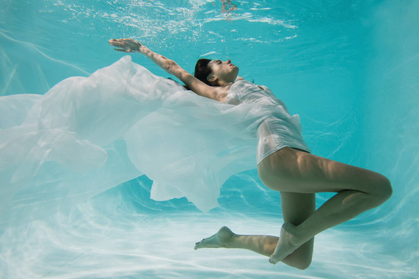 грациозная женщина в белом платье ныряя в бассейне  - Фото, изображение
