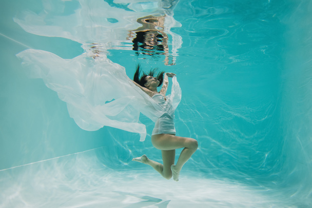 graceful young woman in dress diving in pool with blue water  - Photo, Image
