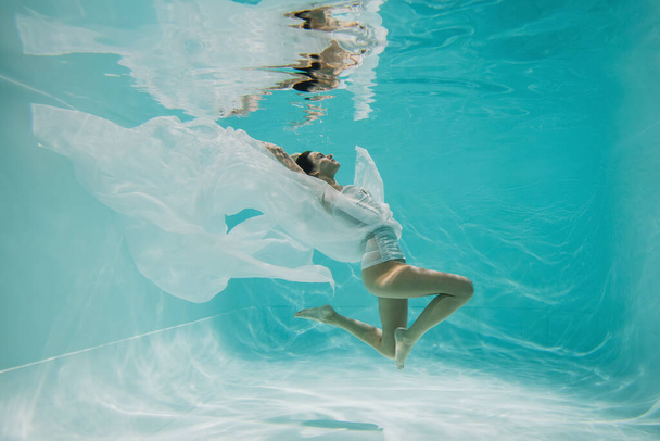 νεαρή γυναίκα με φόρεμα που κολυμπά στην πισίνα με μπλε νερά  - Φωτογραφία, εικόνα