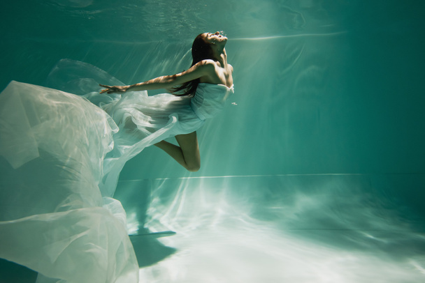 brünette junge Frau in Kleid taucht in Pool  - Foto, Bild