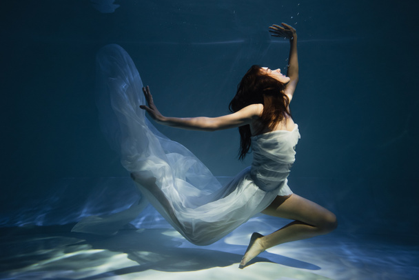 lighting on graceful woman in white elegant dress swimming in pool with blue water - Photo, image