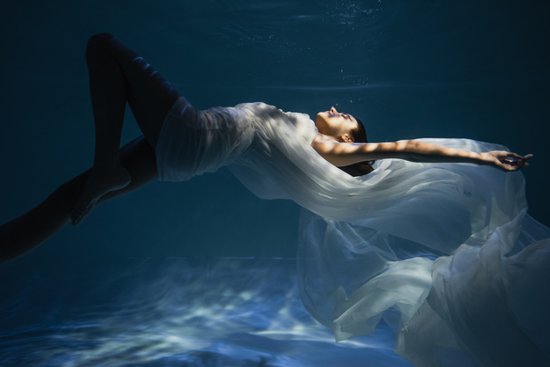 lighting on young barefoot woman in dress swimming in pool with blue water  - Foto, Bild