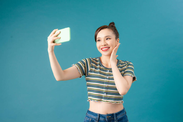 笑顔の女性作る自撮り写真上のスマートフォン上の青の背景 - 写真・画像