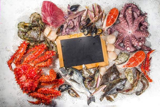 Set van verschillende verse rauwe zeevruchten - octopus, krab, inktvis, garnalen, oester, mosselen, zalm tonijn dorada vis met specerijen van kruiden citroen, witte achtergrond met geplet ijs kopieerruimte bovenaanzicht  - Foto, afbeelding