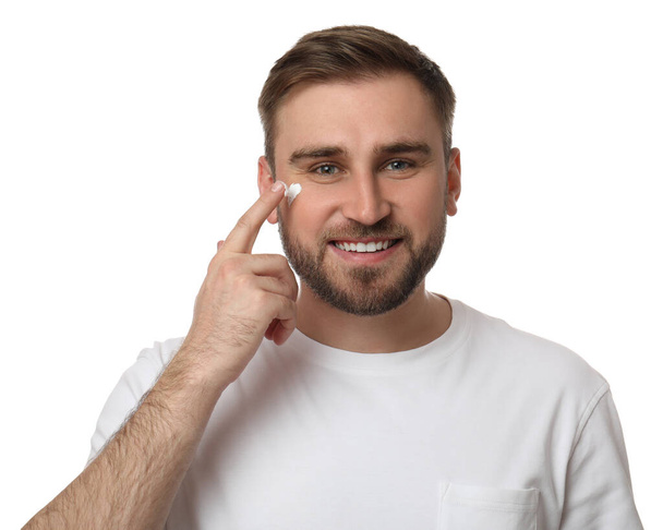 Happy young man applying facial cream on white background - Zdjęcie, obraz
