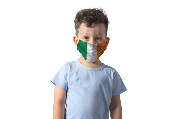 İrlanda bayrağı taşıyan solunum cihazı beyaz çocuk beyaz arka plana izole edilmiş tıbbi maske takıyor.. - Fotoğraf, Görsel