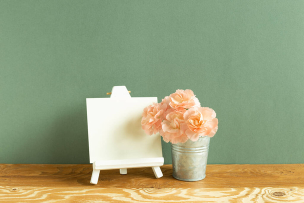 Kolayca ve boş bir tuval ve ahşap masa üzerinde karanfil çiçekleri. yeşil arkaplan - Fotoğraf, Görsel
