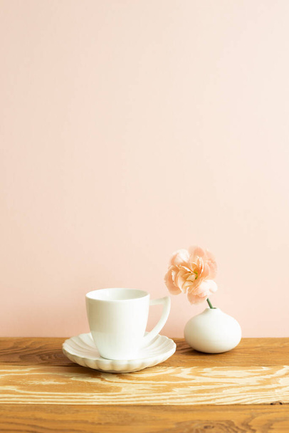White coffee cup with carnation flower on wooden table. pink background - Photo, Image