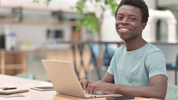 Giovane uomo africano con computer portatile sorridente alla macchina fotografica - Foto, immagini