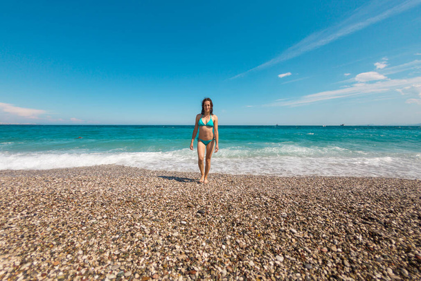 Жінка йде вздовж берега в Анталії, дівчина в купальнику відпочиває на узбережжі моря, морські хвилі і блакитне небо, жінка купається на пляжі.. - Фото, зображення