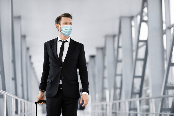 Επιτυχημένος επιχειρηματίας περπατώντας από το αεροδρόμιο, κοιτάζοντας μέσα από το παράθυρο, φορώντας μάσκα - Φωτογραφία, εικόνα