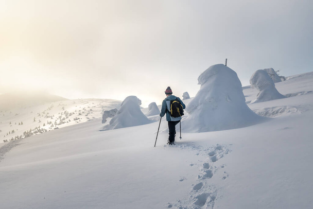 турист гуляет по глубокому сплошному снегу в зимних горах на закате - Фото, изображение