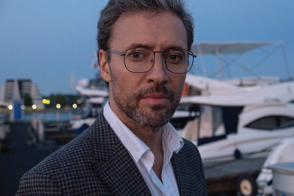 Handsome good-looking mature business man at yacht pier in marina at sunset. - Zdjęcie, obraz
