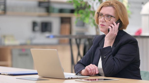 Old Businesswoman with Laptop Talking on Phone in Office - Foto, Imagem