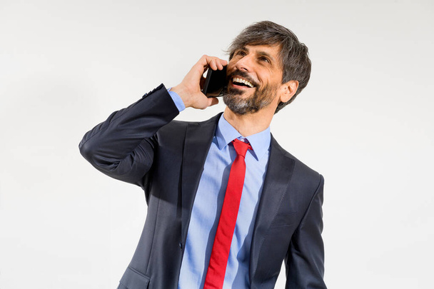 Усміхнений бізнесмен в куртці використовує мобільний телефон і дивиться вгору на білому тлі
. - Фото, зображення