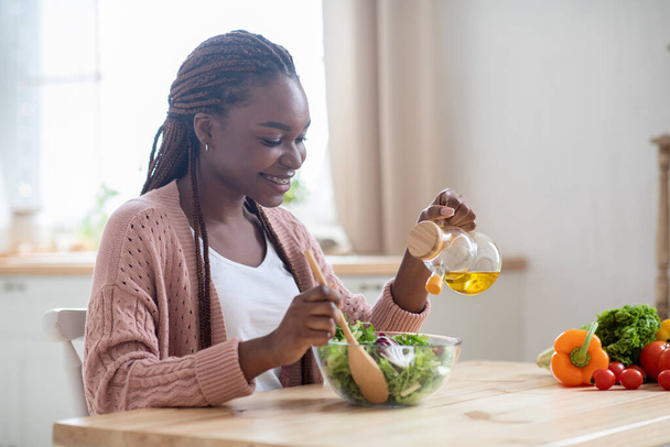 Ευτυχισμένη νεαρή μαύρη κυρία ετοιμάζει υγιεινή σαλάτα λαχανικών στην κουζίνα - Φωτογραφία, εικόνα