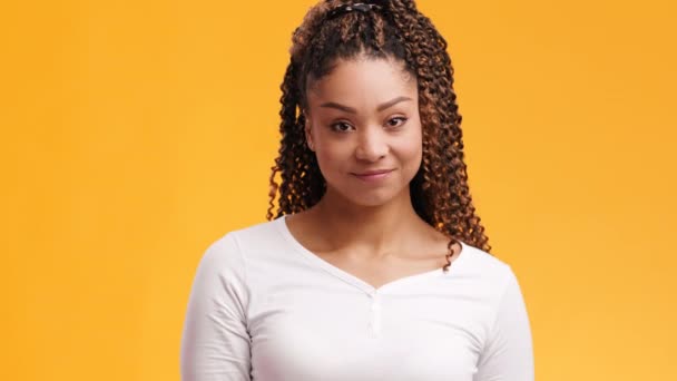 Jeune jolie femme afro-américaine avec une coiffure afro timide et embarrassée, fond orange, ralenti - Séquence, vidéo
