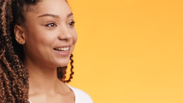 Positiivinen iloinen iloinen nuori afrikkalainen amerikkalainen nainen katselee sivuun ja hymyilee, oranssi tausta, tyhjä tila - Materiaali, video