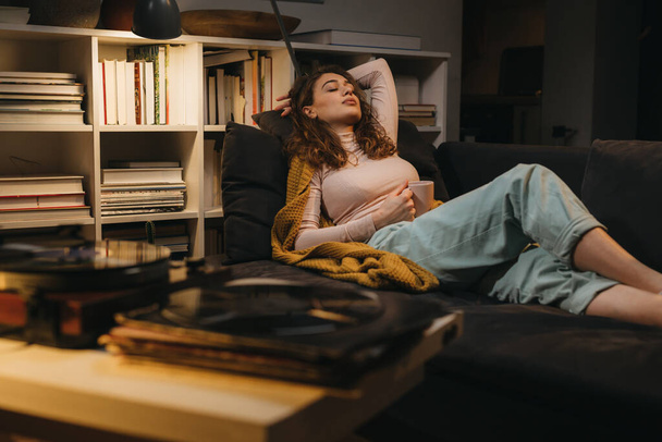 woman relaxing on sofa at her home listening records - Foto, afbeelding