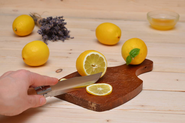 mano con cuchillo corte limones sobre mesa de madera - Foto, imagen