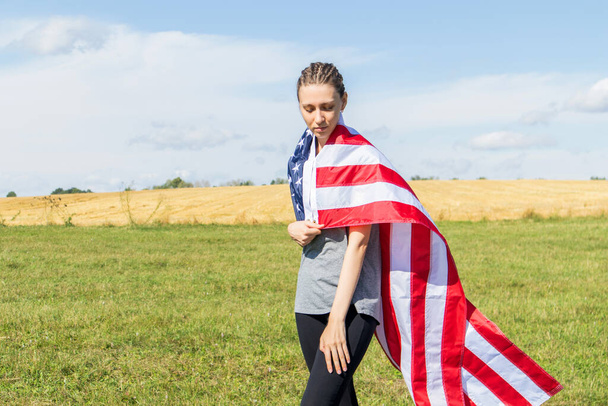 Αμερικανίδα νεαρή γυναίκα με αφρο-κοτσίδες σε ένα χωράφι τυλιγμένο σε σημαία ΗΠΑ. - Φωτογραφία, εικόνα