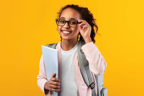 Alegre joven negro chica sosteniendo libros de texto mirando a la cámara - Foto, imagen