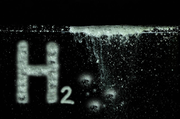 letras de hidrógeno h2 y muchas pequeñas burbujas blancas en agua negra - Foto, Imagen