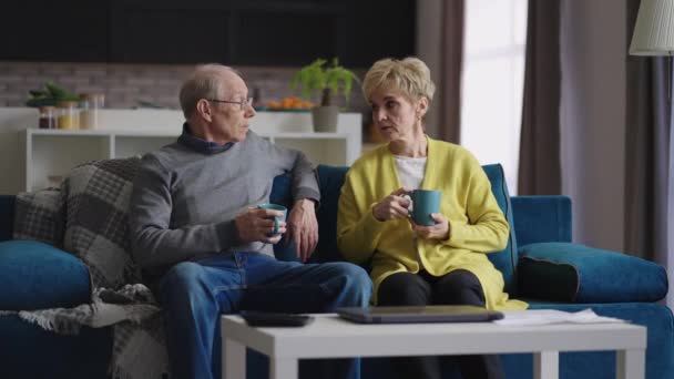 manželé pár důchodců odpočívá doma o víkendu, starý muž a žena sedí na gauči v obývacím pokoji bytu - Záběry, video