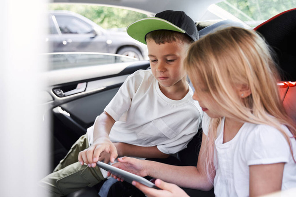 Cute siblings using digital tablet in car - Fotó, kép