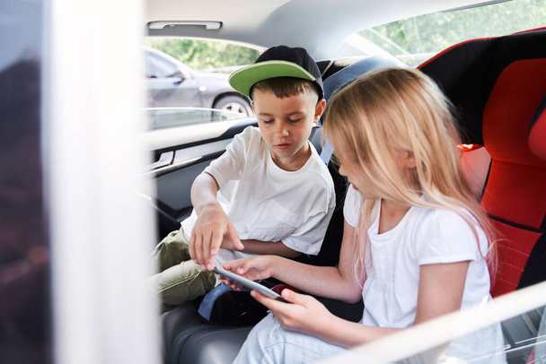 Merry brother and sister playing on tablet in car - Foto, Bild