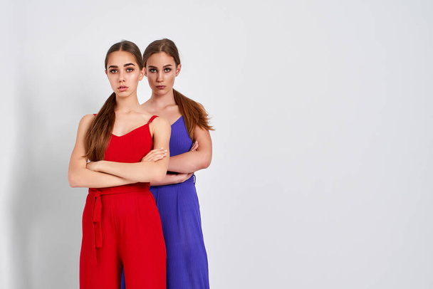 Two girls standing in studio in elegant colorful overalls on white background - Foto, afbeelding