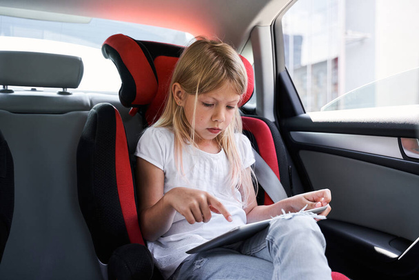 Μικρό χαριτωμένο κορίτσι χρησιμοποιώντας tablet στο αυτοκίνητο - Φωτογραφία, εικόνα