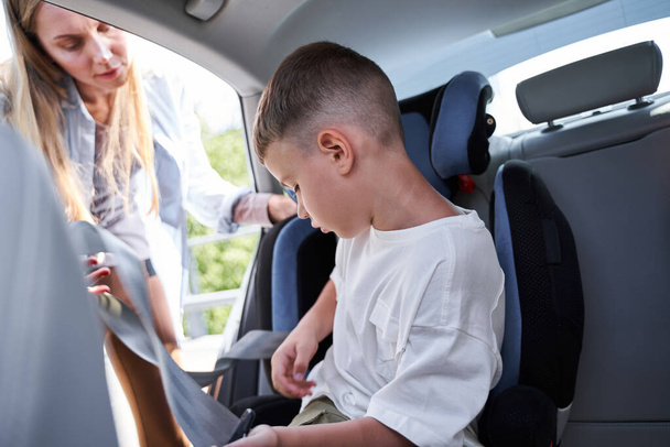 Attentive woman taking care of son in car - Photo, image