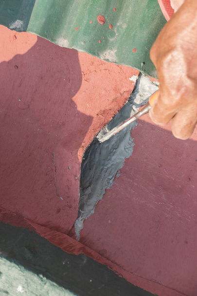 A man adds polyurethane roof sealant underneath one of the metal sheets of a gutter. DIY repair project at home. - Photo, Image