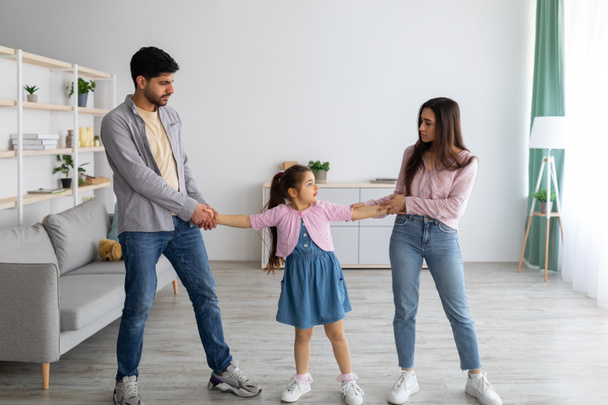 Concetto di divorzio. I genitori arabi litigano per il loro bambino, l'uomo pazzo e la donna litigano, in piedi in soggiorno - Foto, immagini
