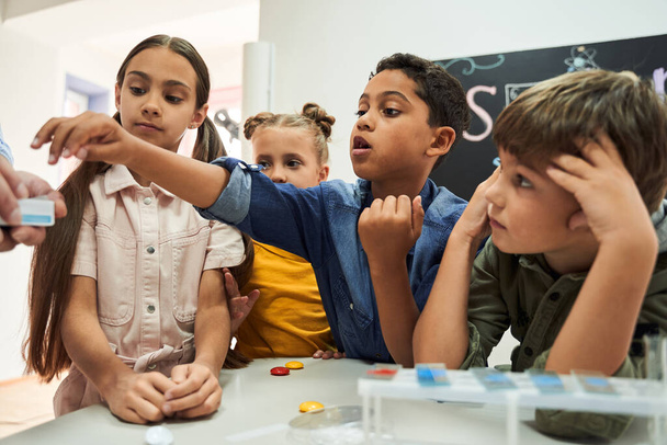 Inquisitive multiracial boy reaching for a test glass to study chemistry - 写真・画像