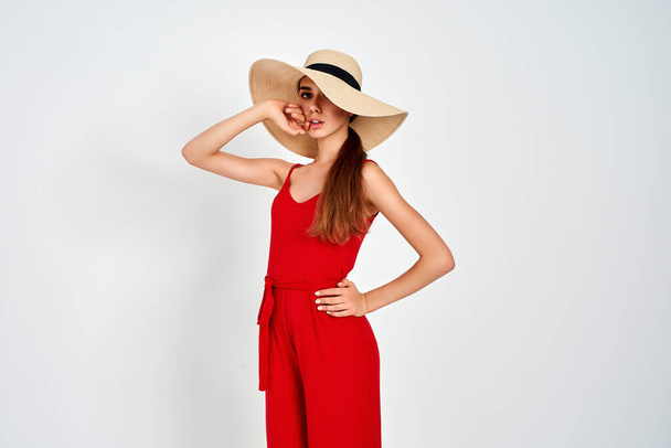 Beautiful girl in sun hat standing on white background in studio in elegant red overall - Foto, Imagen