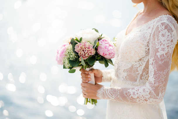 Невеста в белом кружевном платье держит букет розовых пионов в руках - Фото, изображение