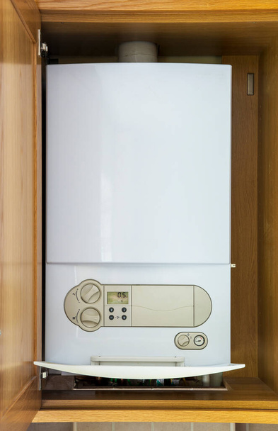 Ένας λέβητας συμπύκνωσης με καύσιμο φυσικό αέριο για οικιακή κεντρική θέρμανση και σύστημα άμεσου ζεστού νερού τοποθετείται μέσα σε ξύλινο ντουλάπι για να το αποκρύψει. - Φωτογραφία, εικόνα