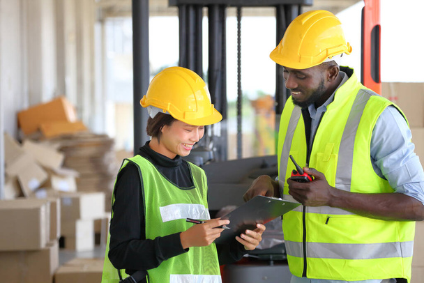 Afro-Amerikaanse en Aziatische werknemers dragen veiligheidsvest tijdens het werken in magazijn controleren op de inventaris met behulp van digitale tablet - Foto, afbeelding