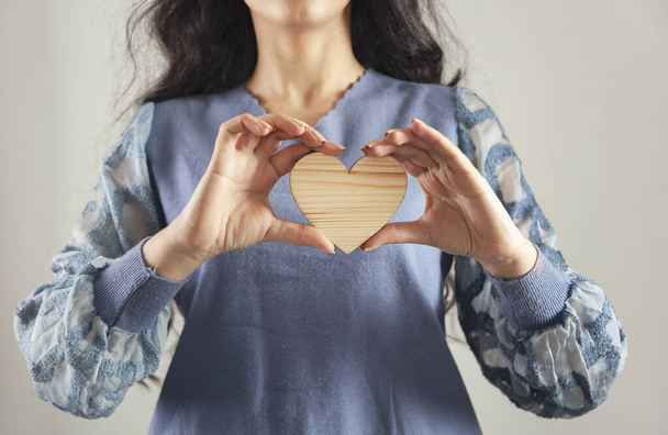Young woman holding wooden heart sign. - Fotografie, Obrázek